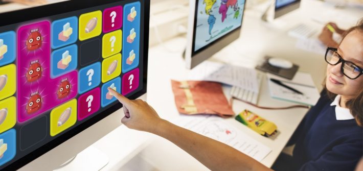 dos niños se encuentran en la sala de computación apuntando a un juego que aparece en la pantalla de un computador