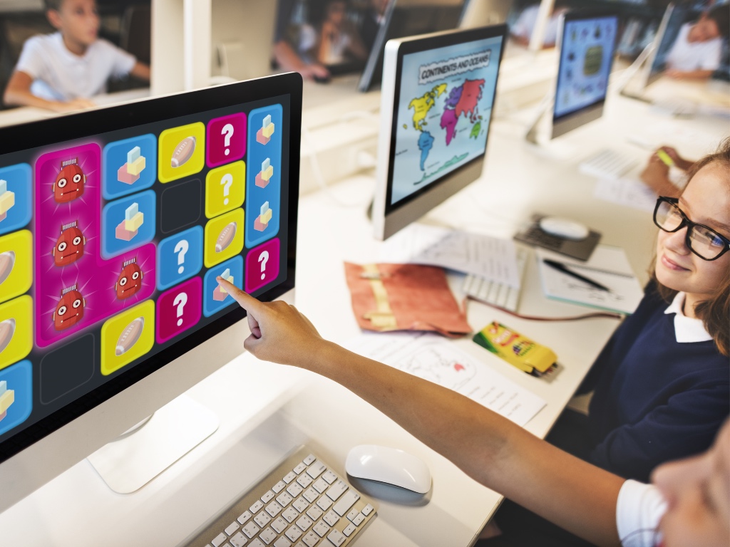 dos niños se encuentran en la sala de computación apuntando a un juego que aparece en la pantalla de un computador