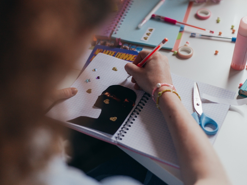 manos de una joven sobre un cuaderno donde realiza un collage