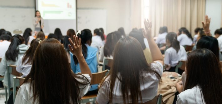 estudiantes levantando la mano dentro del aula